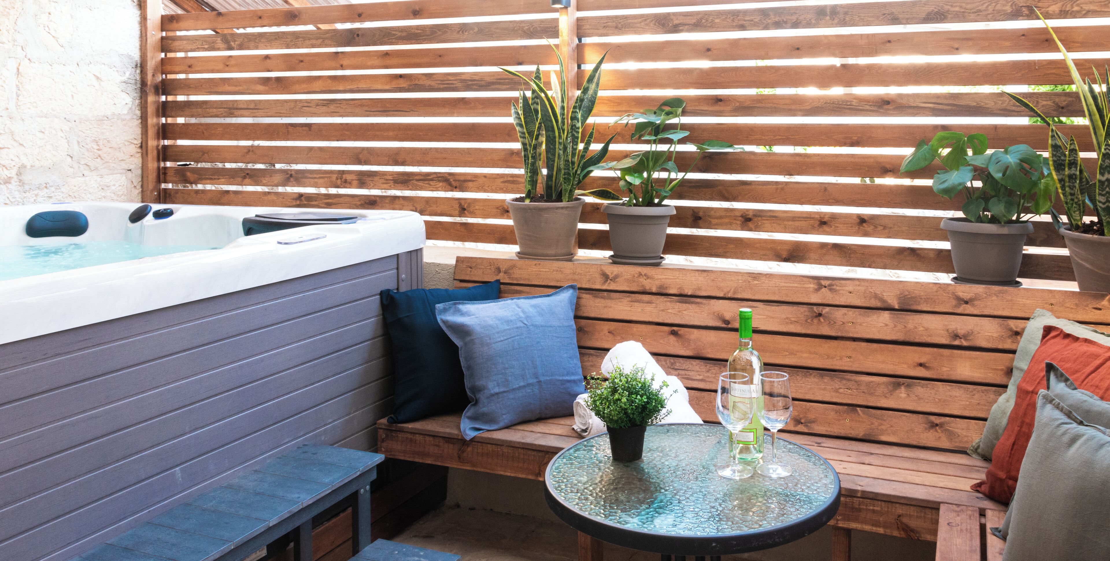 Un bain à remous, un banc en bois, des plantes en pot et une table avec des verres à vin.