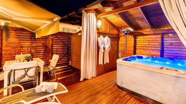 Une terrasse en bois avec un jacuzzi, une table et des chaises, ainsi qu’un espace salon couvert.
