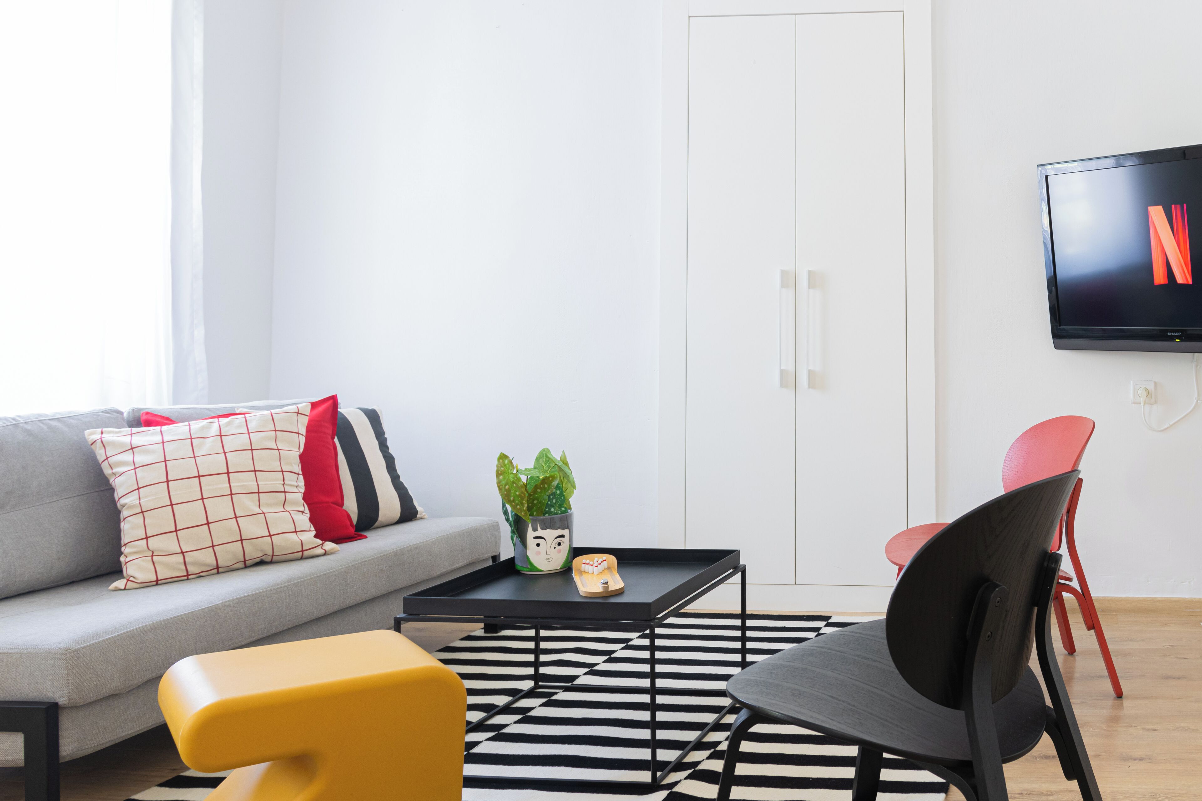 A modern living room with a sofa, a coffee table, a yellow chair, and a TV mounted on the wall.