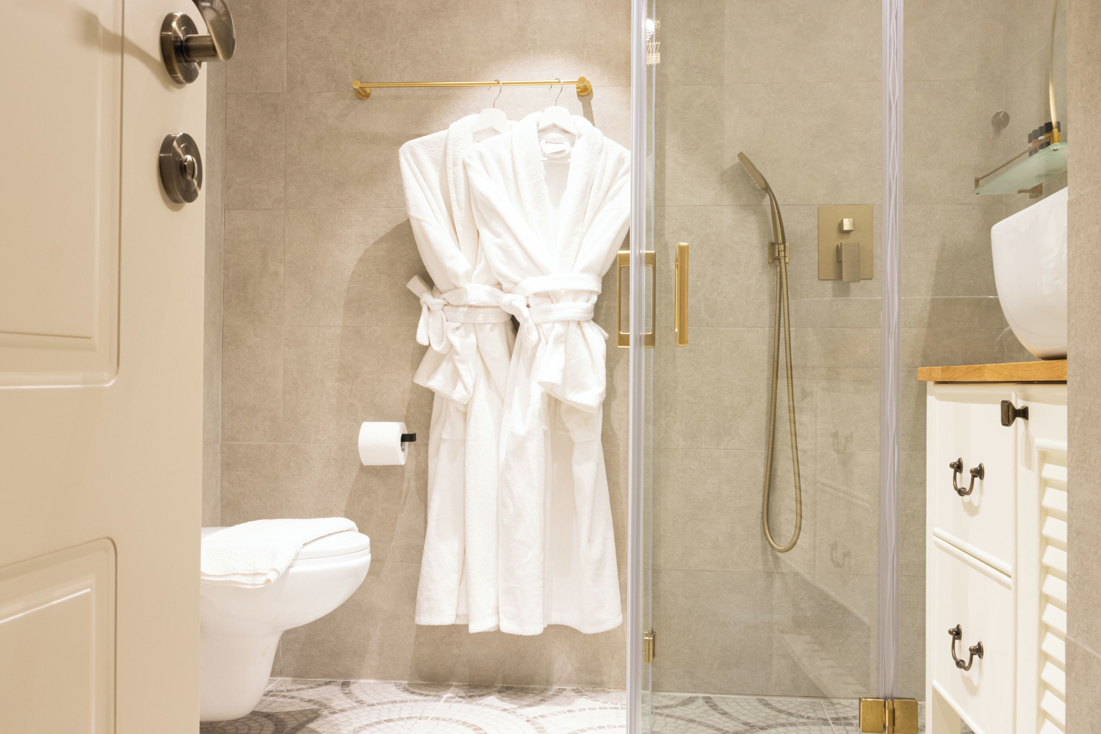 A bathroom with a glass shower enclosure, a white toilet, and a white robe hanging on a towel rack.