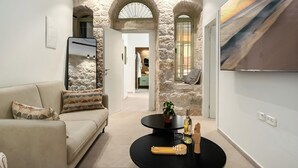 Un salon moderne avec une arche en pierre, un canapé, une table basse avec une bouteille et des verres, et un tableau accroché au mur.