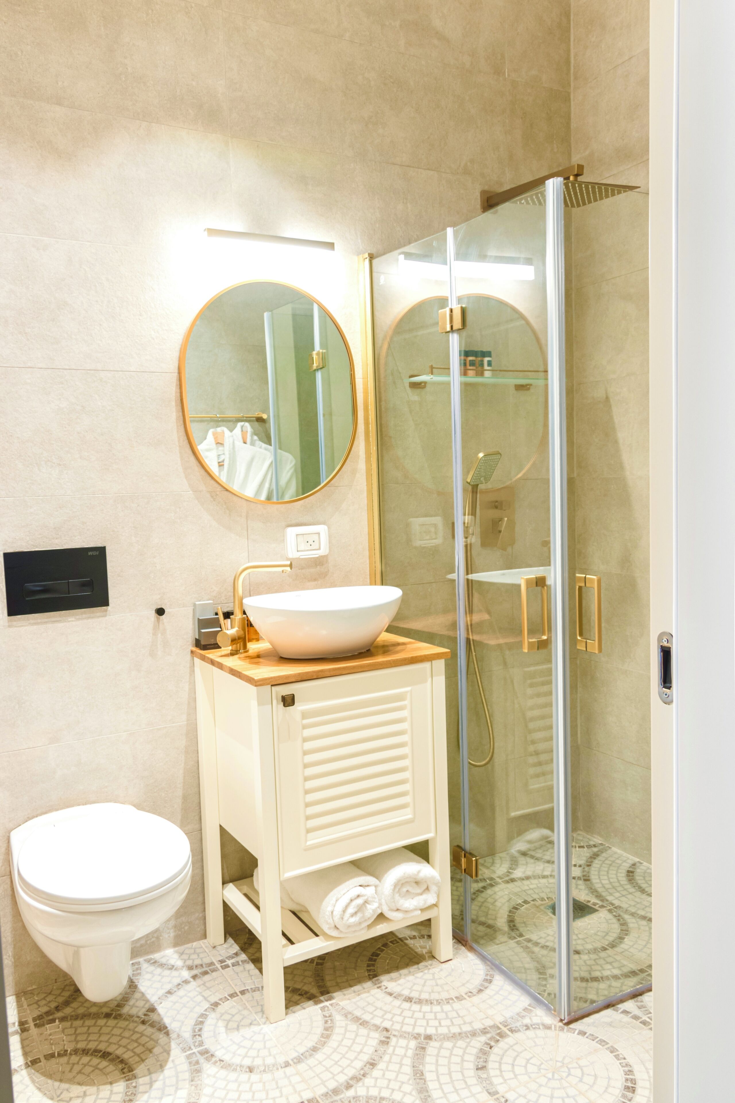 A modern bathroom with a round mirror, a white sink, a toilet, and a glass-enclosed shower area.