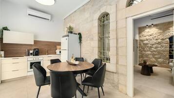 Eine moderne Küche mit einem runden Holztisch und schwarzen Stühlen, einem weißen Kühlschrank sowie einer Steinwand.