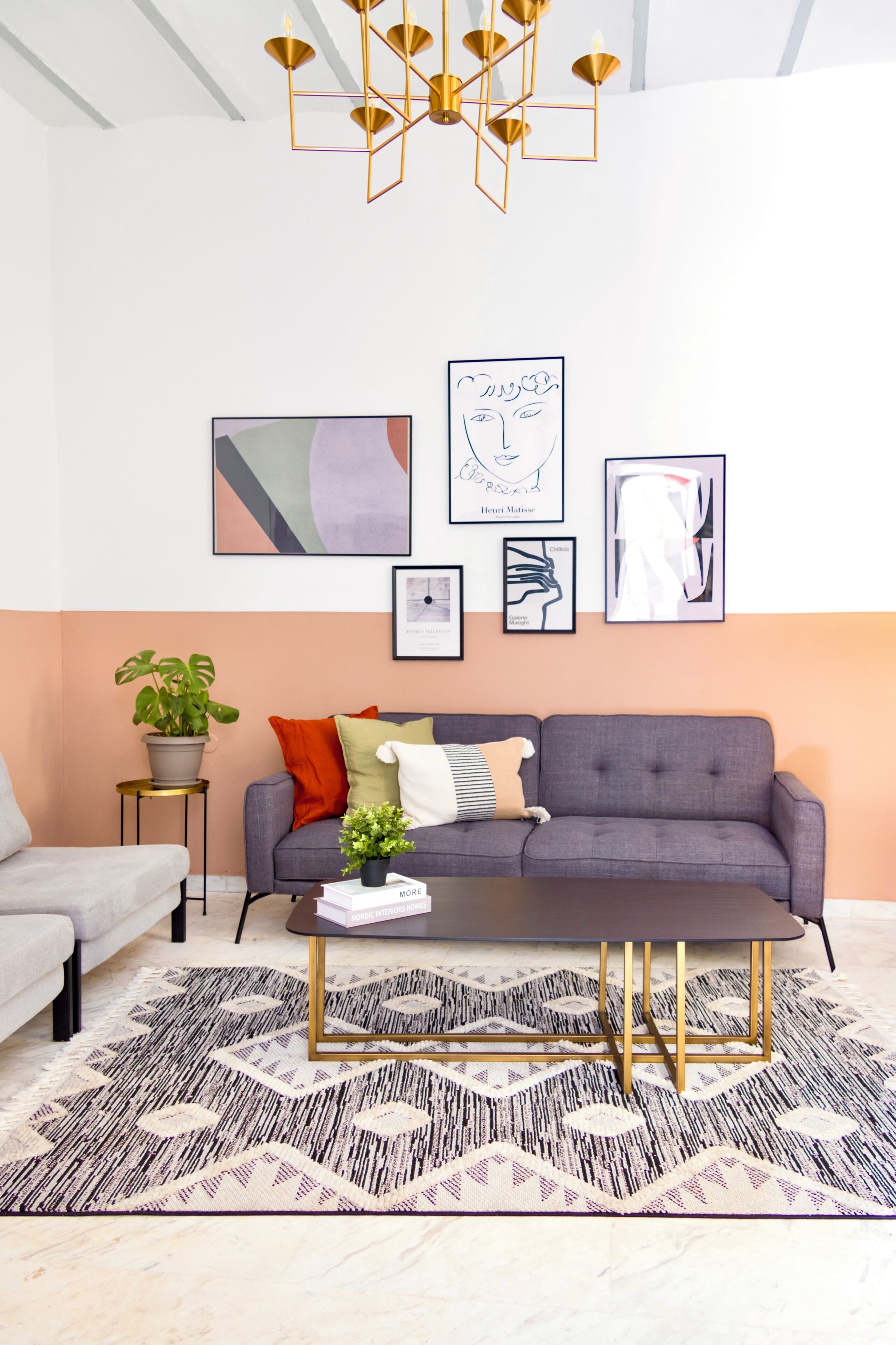 Ein modernes Wohnzimmer mit einem grauen Sofa, einem gemusterten Teppich und einem geometrischen Kronleuchter.