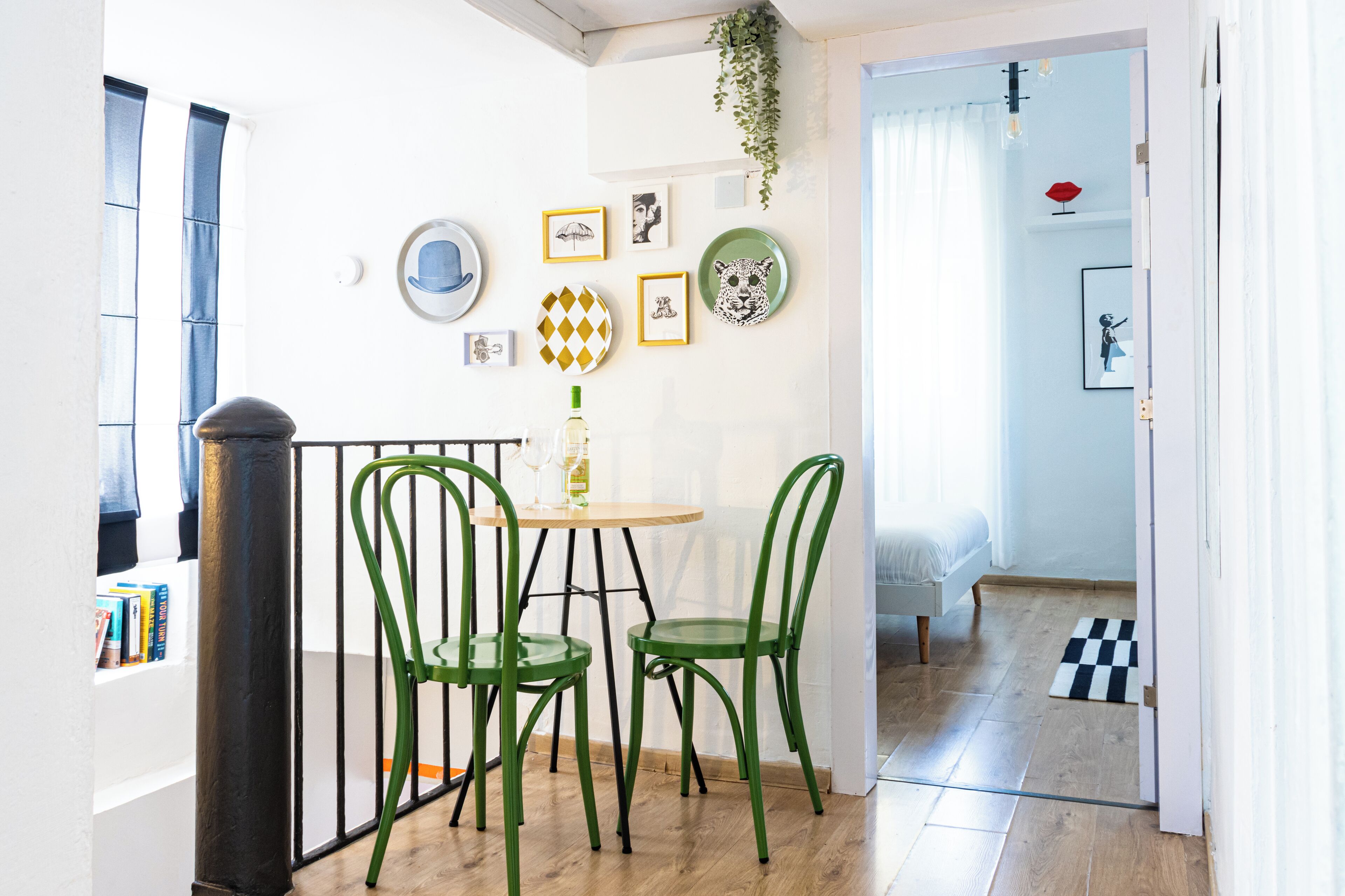 A dining area with a round table, two green chairs, and a small vase with a glass.