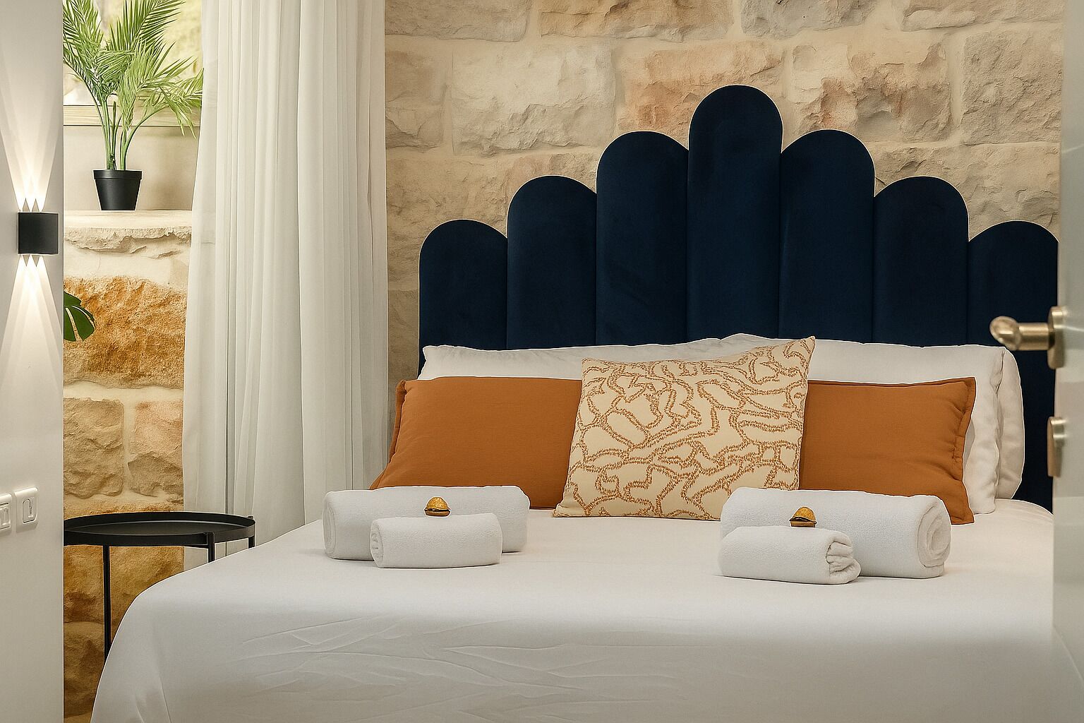 A hotel room with a stone wall, a bed with a unique headboard, and a potted plant.