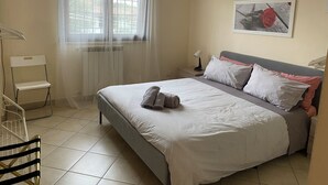 Una camera da letto ordinata con un letto, una sedia, un termosifone e una finestra con tende.