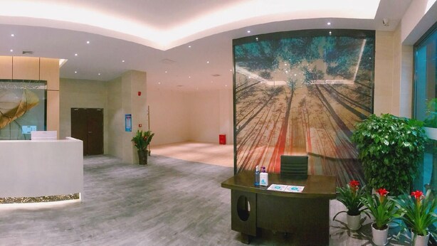 A reception area with a reception desk, a large wall mural, and potted plants. - Green Tree Inn Zhixuan Hotel (Nanning)