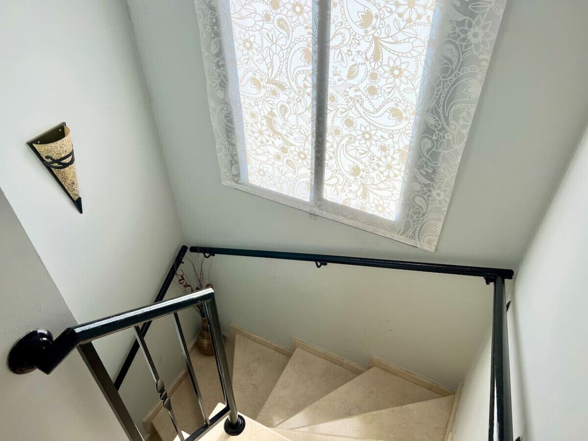 A staircase with a metal handrail, a patterned window, and a wall-mounted decoration.