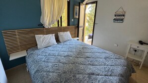 Une chambre à coucher avec un lit, une table de chevet, une lampe suspendue et une vue sur l’extérieur.