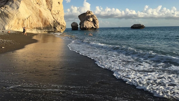 Une plage avec une grande formation rocheuse et une mer calme.
