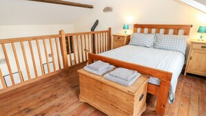 A wooden-framed bed with a checkered bedspread, two bedside tables with lamps, and a wooden chest of drawers with folded towels. - The Hay Barn (High Peak)