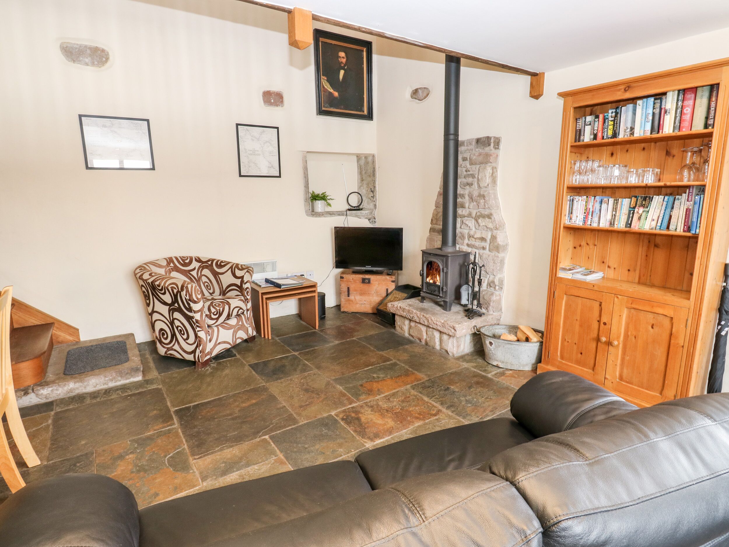 A cozy living room with a stone fireplace, a sofa, a television, and a bookshelf.