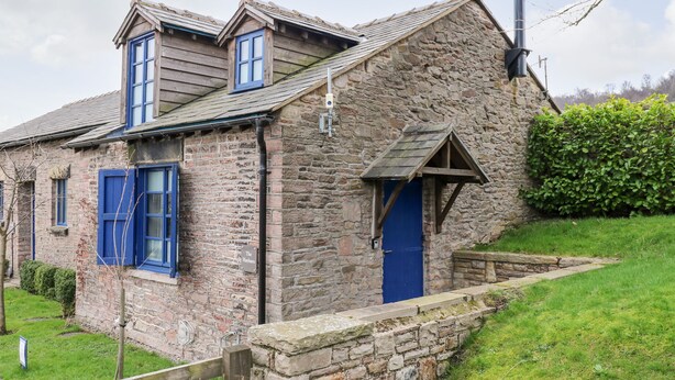 A stone house with a blue door and windows, a chimney, and a small garden area. - The Hay Barn (High Peak)