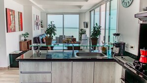 A modern kitchen with a glass island, stainless steel appliances, and a large window offering a view. - Playa Cartagena (Cartagena)