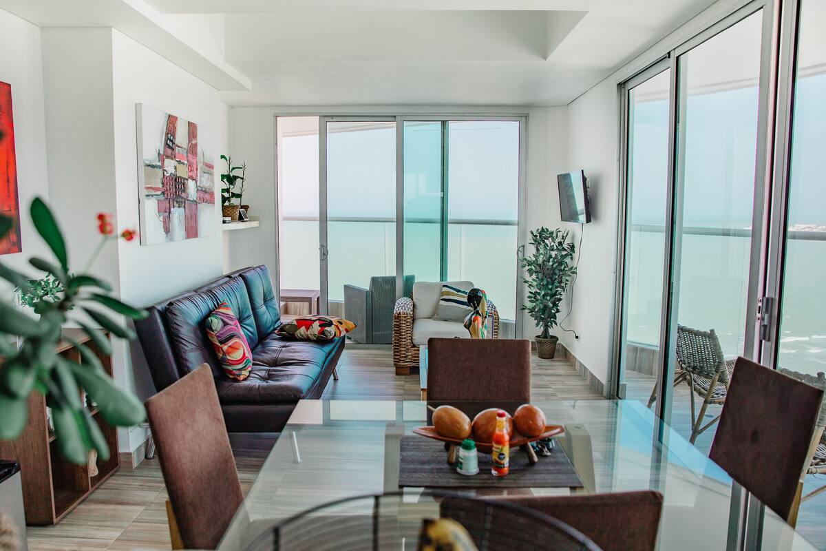A modern living room with a glass dining table, leather sofa, and a balcony with a view.