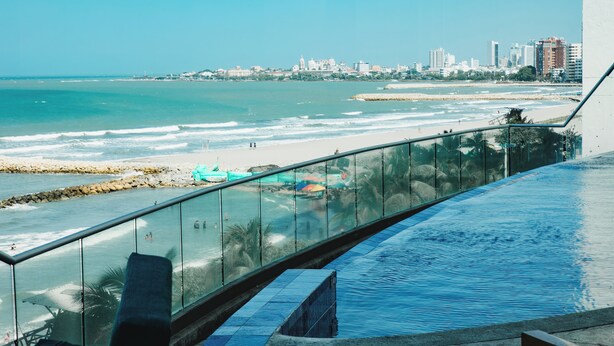 A pool with a glass railing overlooking a beach and city skyline. - Playa Cartagena (Cartagena)