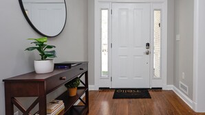 Un pasillo con una puerta blanca, una consola de madera con una planta en maceta y un felpudo negro.