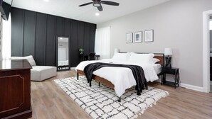 Un dormitorio moderno con cama, mesitas de noche, ventilador de techo y un gran ventanal.