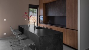 Una cocina moderna con una isla central, taburetes de bar y una pared de piedra visible a través de la ventana.