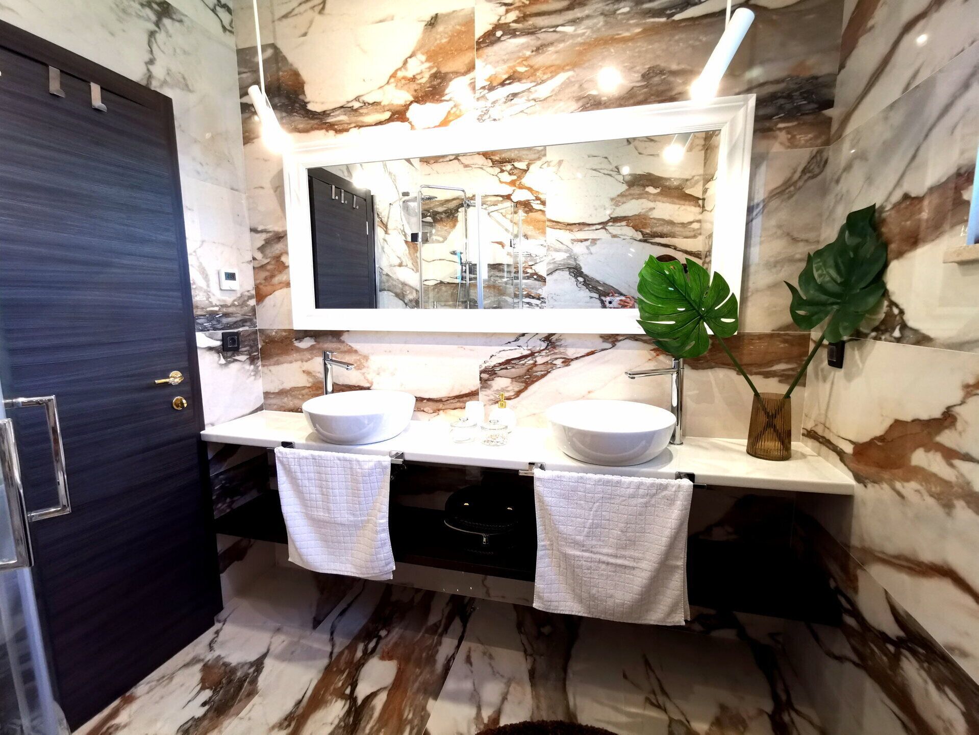 Un baño con dos lavamanos, un espejo grande y paredes con diseño de mármol.