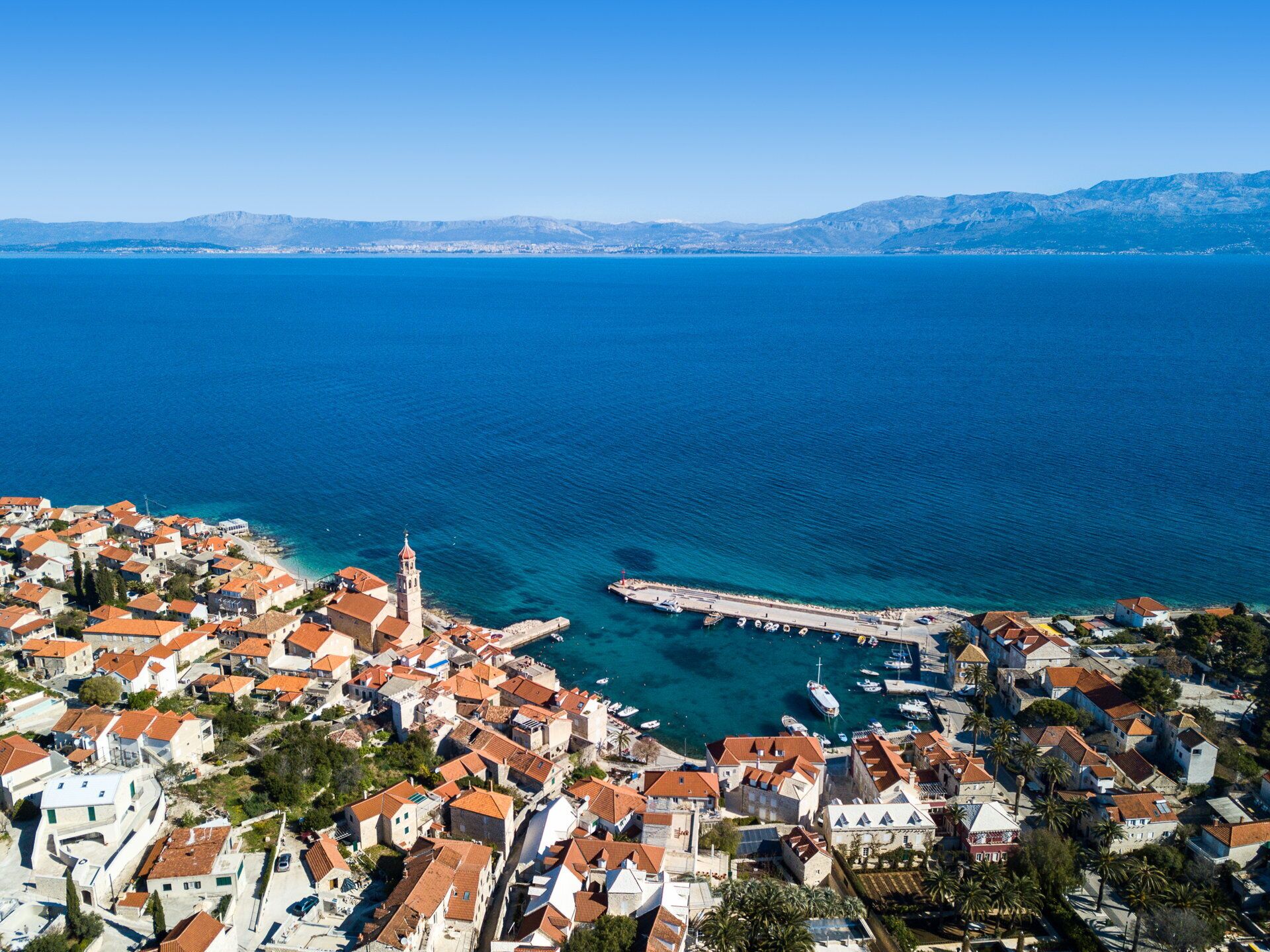 A coastal town with a prominent church tower, a marina, and a clear view of the sea.