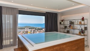 A modern bathroom with a glass-enclosed hot tub, a wooden vanity, and a view of a coastal town. - Luxury Villa Persephone with Pool (Makarska)