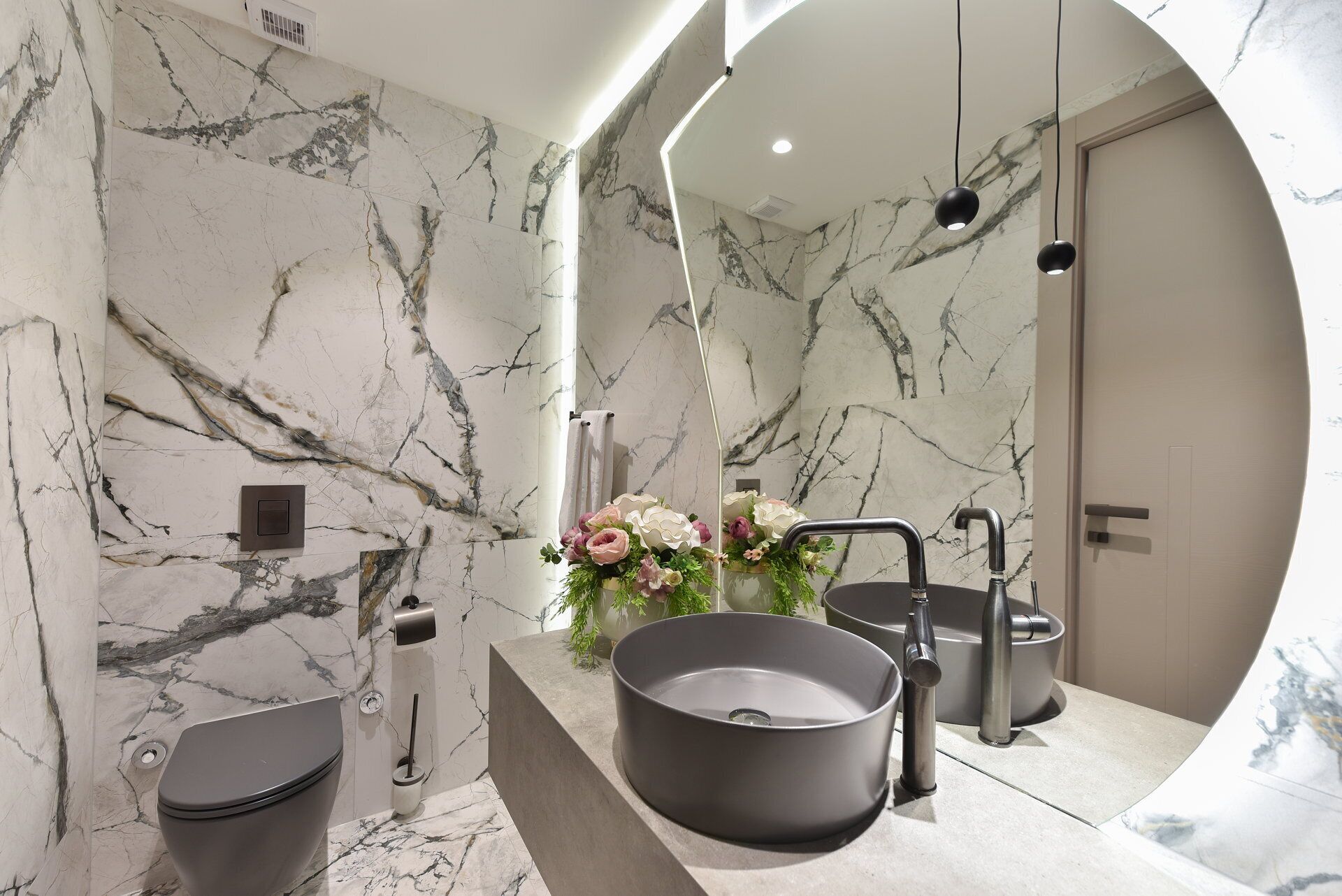 Une salle de bain moderne avec un pare-baignoire en marbre, un lavabo rond, des toilettes et un espace douche.