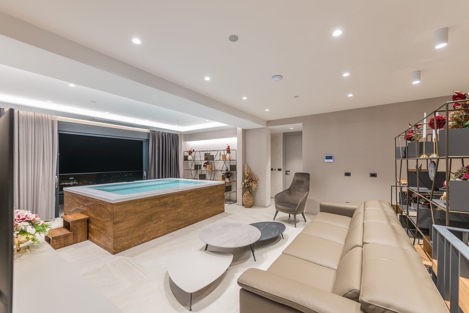 A modern living room with a pool, a sofa, a chair, and a bookshelf.