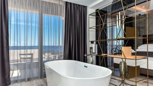 A modern hotel room with a large bathtub, a glass partition with a geometric frame, and a view of the sea through sheer curtains. - Luxury Villa Persephone with Pool (Makarska)