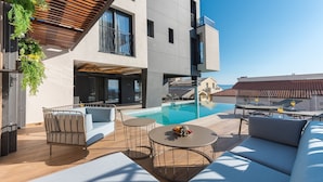 A modern outdoor pool area with a sofa, two round tables, and a dining table. - Luxury Villa Persephone with Pool (Makarska)