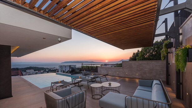 Una terraza en la azotea con piscina, zona de estar y vistas al atardecer sobre el mar.