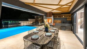 Un área interior de piscina moderna con una mesa de comedor preparada para seis personas, rodeada de sillas, y una chimenea al fondo.