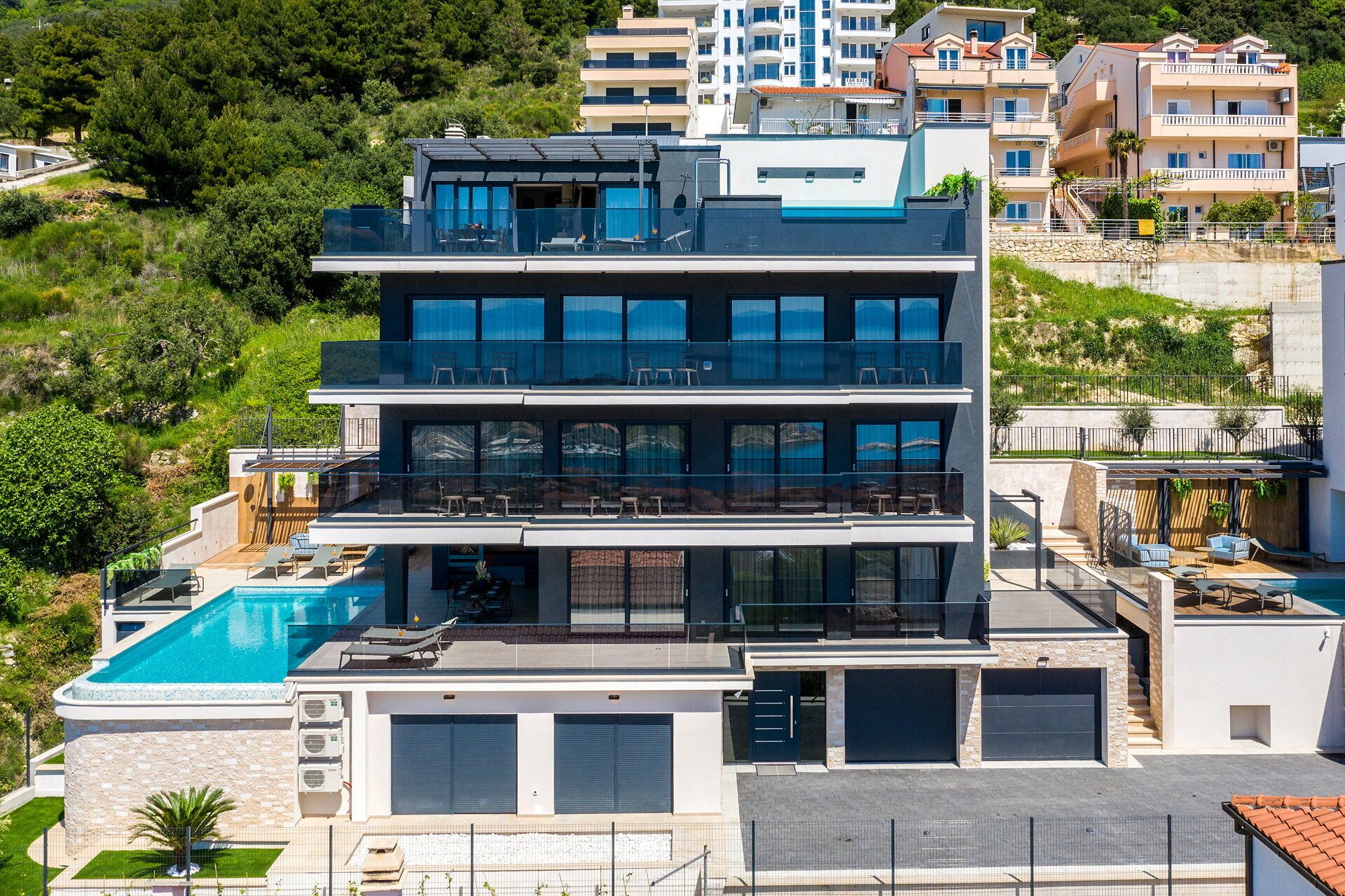 A modern multi-story building with a rooftop pool, large windows, and a balcony with outdoor seating.