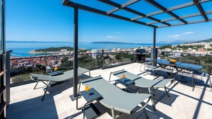 Terraza en la azotea con sillones y una mesa, con vistas a un paisaje urbano costero.