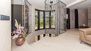 Un interior moderno con una escalera curva, un jarrón grande de flores y un sofá color beige.