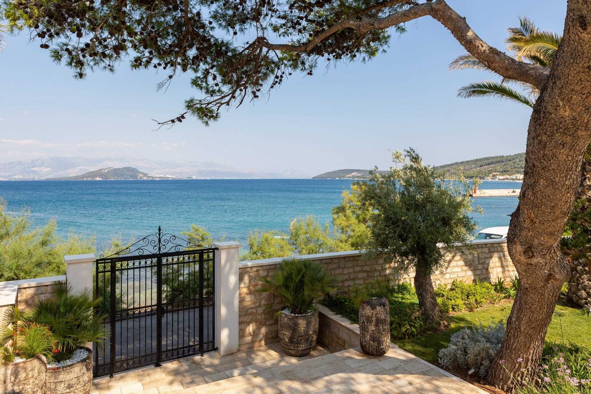 A coastal property with a stone wall, a metal gate, and a view of the sea.