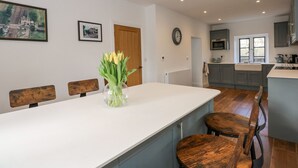 A modern kitchen with grey cabinets, a white countertop, and a wooden dining table with four chairs. - Kylemore Railway Cottage (Stamford)