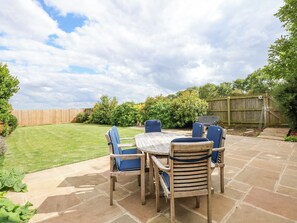 An outdoor patio with a round table and six chairs, surrounded by a wooden fence and lush greenery. - Kylemore Railway Cottage (Stamford)