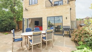 A two-story house with a patio area featuring a table and chairs, a barbecue grill, and a large sliding glass door leading to an indoor space. - Kylemore Railway Cottage (Stamford)
