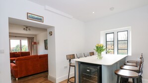 A modern kitchen with a central island, bar stools, and a dining area with a red sofa. - Kylemore Railway Cottage (Stamford)