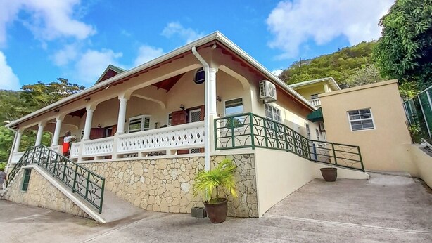 A two-story building with a porch, stone walls, and a green railing. - The Grenada Escape (Saint George)