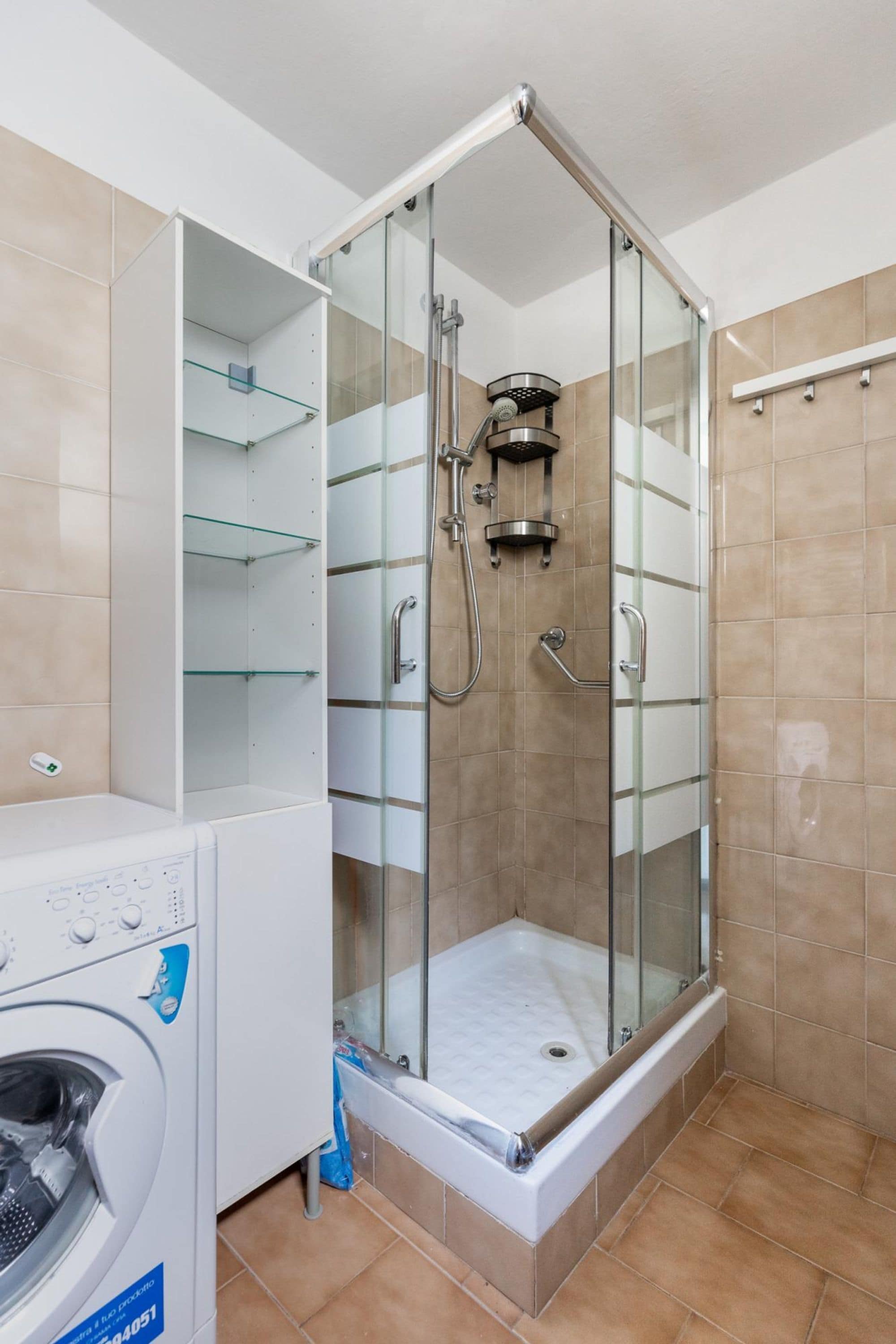 Une salle de bain moderne dotée d’une douche à parois de verre, d’un lave-linge encastré et d’une étagère en verre.