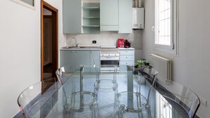 A modern kitchen with a glass dining table, white cabinets, and a built-in oven. - Appartamento Alla Finestrella by Wonderful Italy (Bologna)