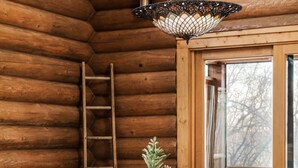 L’intérieur d’un chalet en bois, avec une table et des chaises, un luminaire suspendu et une fenêtre donnant sur les arbres.