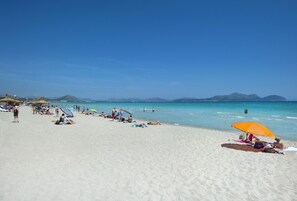Ein Strand mit badenden Personen, einem klaren Himmel und Bergen im Hintergrund.