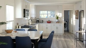A modern kitchen with white cabinets, a built-in stove, and a dining area with blue chairs. - Aviation Landing Vacation Homes Fallbrook CA (Fallbrook)