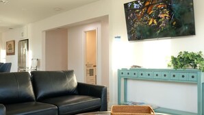 A modern living room with a black leather sofa, a glass coffee table, and a teal console table with a plant. - Aviation Landing Vacation Homes Fallbrook CA (Fallbrook)