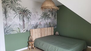 A bedroom with a green wall, a mural of tropical plants, a wooden headboard, a green bedspread, a woven hanging light, and a small stool. - 4-bedroom house in Terre d'Iroise (Lanildut)