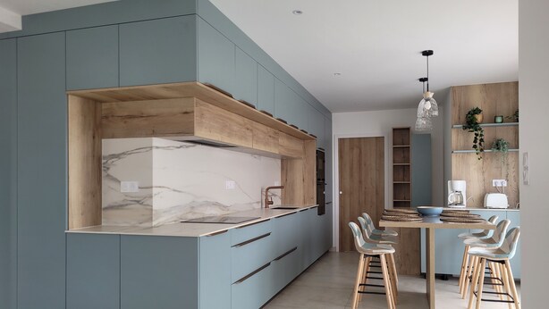 A modern kitchen with light blue cabinetry, a marble countertop, and a wooden dining area with chairs and a table. - 4-bedroom house in Terre d'Iroise (Lanildut)